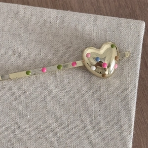 Close-up of golden metal hairpin with colorful polka dots and heart-shaped detail