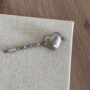 Detailed view of heart-shaped metal hair clip with colorful enamel polka dots on fabric