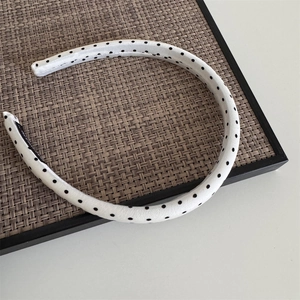 U-shaped white headband with black polka dots on a textured tray, minimalist hair accessory
