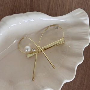Détail d'une barrette noeud dorée avec perle et cristaux dans un plat en coquillage