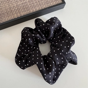 Detailed view of a black silk-like scrunchie with white polka dots on a minimalist white base