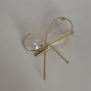 Détail de la pince à cheveux nœud doré avec perle blanche et petits strass brillants
