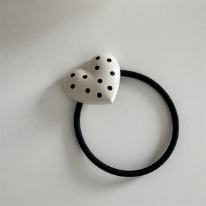 Detailed view of black elastic hair tie featuring a white heart charm with black polka dots