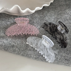 Détail de trois pinces à cheveux à motif dentelle rose, blanc et noir sur fond tricoté