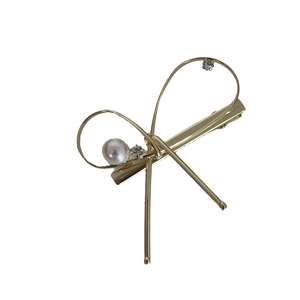 Barrette à cheveux nœud doré avec perle blanche et cristaux brillants sur fond blanc