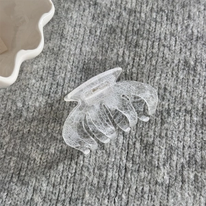 Détail d'une pince à cheveux transparente avec motif dentelle blanche sur tissu tricoté