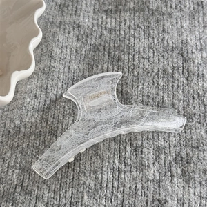 Détail montrant la texture en dentelle d'une pince à cheveux blanche translucide sur tissu gris