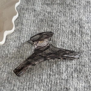 Détail d'une grande pince à cheveux grise avec motif dentelle noire sur fond en tricot