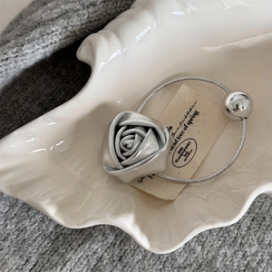 Detailed close-up of metallic silver rose hair tie with elastic band on a ceramic dish