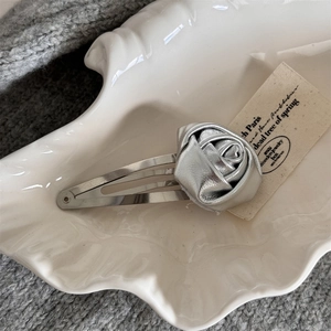 Detailed macro view of silver metallic rose hair clip on textured ceramic tray