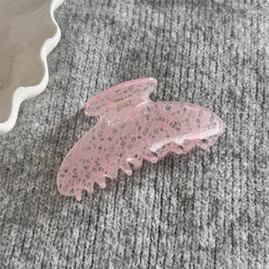 Gros plan d'une pince à cheveux rose avec motif dentelle et ressort doré sur tricot gris
