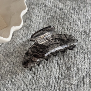 Détail d'une pince à cheveux grise à motif dentelle sur fond de tissu texturé doux