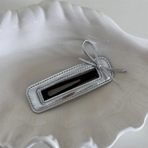 Close-up of a silver metallic bow hair clip featuring fine stitching on a ceramic shell tray