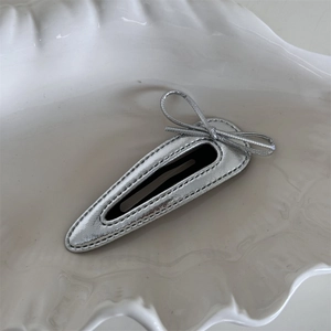Detailed view of silver metallic leather bow hair clip on a white ceramic plate