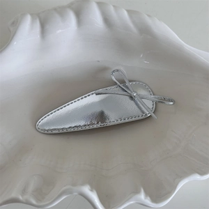 Detail shot of silver metallic leather bow hair clip with fine stitching on white plate