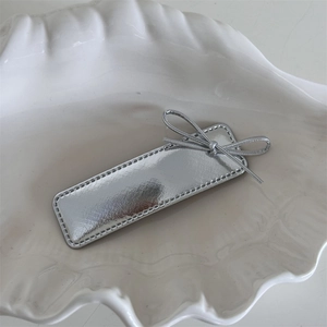 Detail view of silver leather bow hair clip with fine stitching on a shell tray