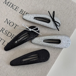Set of four silver and black glitter hair clips with ribbon bows on fabric background