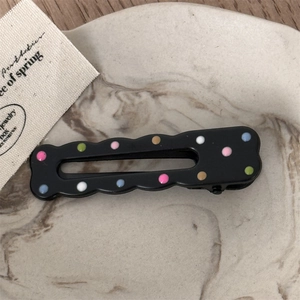 Detail of black resin hair clip with colorful polka dots on a marble tray