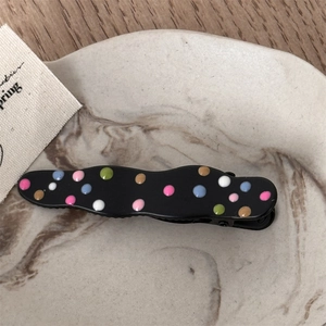 Close-up of black wavy metal hair clip with colorful polka dots on marble tray