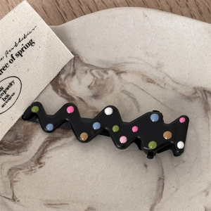 Macro view of black wave-shaped hair clips with colorful polka dots on a marble tray