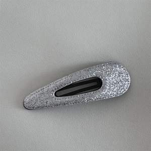 Close-up of a silver glitter teardrop BB hair clip on a gray leather background