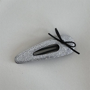 Detail of silver sequined BB hair clip with black thin string bow on leather background