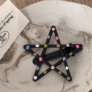Detail of star-shaped black metal hair clip with colorful polka dots on a marble tray