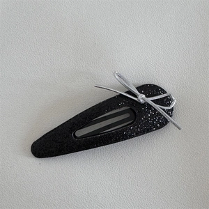 Detail of a black glitter teardrop snap hair clip featuring a small silver ribbon bow knot