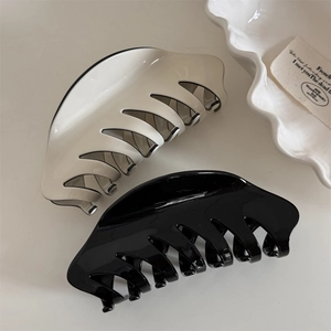 Top view of large glossy acrylic hair claws in black and cream on a minimalist tray