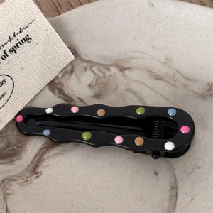 Detail of wavy black metal hair clip with colorful enamel polka dots on marble background