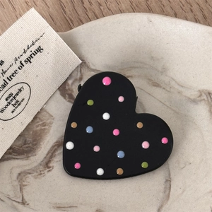 Detail of a matte black heart-shaped hair clip with colorful dots on a marble tray