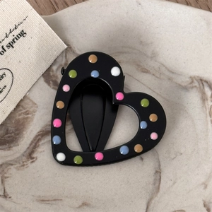 Close-up of heart-shaped black hair clip with colorful polka dots on marble tray