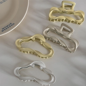 Detail of large matte wave hair claws in soft yellow and cream with metal springs