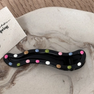 Close-up of wavy black metal hair clip with colorful dots on a marble plate