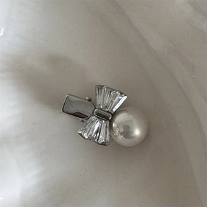 Détail macro d'une barrette à nœud argentée avec cristaux et une grande perle blanche