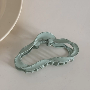 Detail view of light green wave-shaped hair claw clip with realistic stitching texture