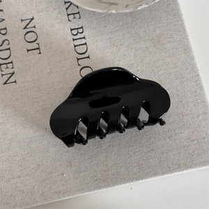 Close-up of a large glossy black French hair claw clip on neutral linen fabric texture