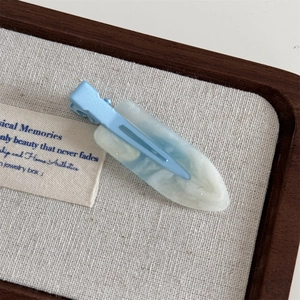 Detail of light blue matte hair clip with translucent resin on a wooden jewelry tray