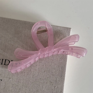 Détail de la pince à cheveux noeud rose translucide avec ressort doré sur tissu