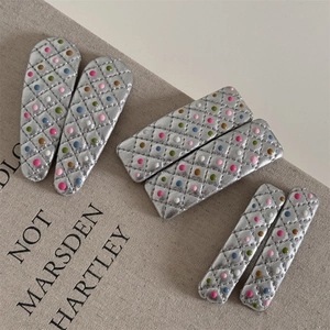 Détail de barrettes en similicuir argenté avec motif matelassé et pois colorés en relief