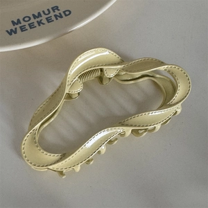 Detail of a wavy cream alloy hair claw clip with stitch-textured edges and metal spring
