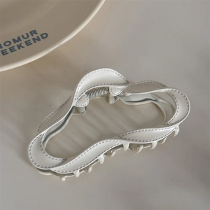 Detail of cream wavy hair claw clip with unique stitching texture and silver metal spring