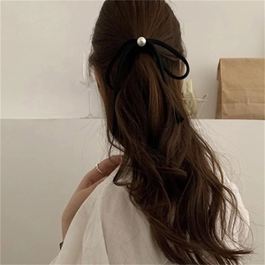 Elegant black bow hair tie with white pearl pendant worn in a low ponytail style