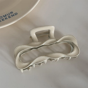 Close-up of cream-white alloy hair claw with unique stitched texture and wave design