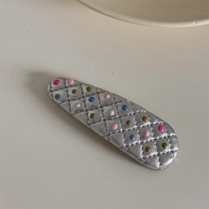 Détail de la pince BB en cuir argenté avec motif matelassé et pois colorés