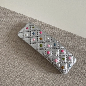 Détail de la barrette en cuir argenté matelassé avec des pois colorés et forme rectangulaire