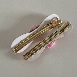 Dettaglio di fermagli per capelli con fiocco rosa, bordo bianco e clip a becco in oro