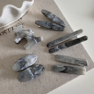 Detail of small ink grey marble hair clips on beige linen with acetate texture
