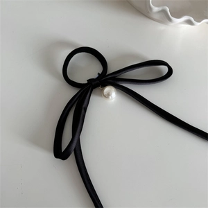 Detail view of black satin bow hair tie featuring a polished white pearl pendant decoration