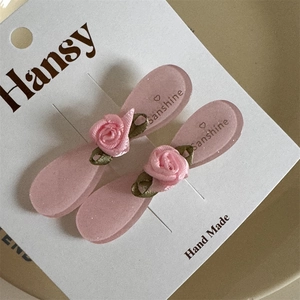 Dettaglio della rosa in tessuto rosa e delle foglie verdi sulle mollette per capelli